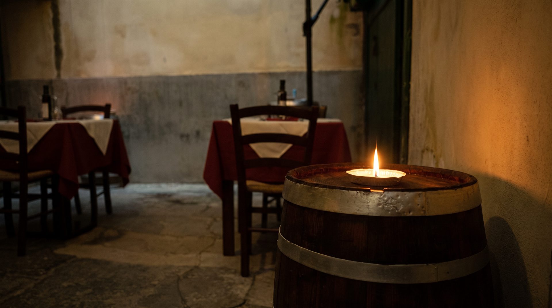 La porta del ristorante nel vicolo, la sera: il telaio verde della porta e i tavoli con le tovaglie rosse, illuminati da una candela.